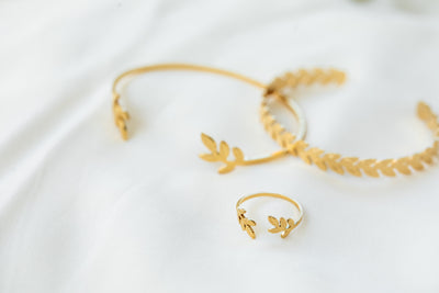 טבעת עלים וצמיד עלים זהב על רקע סדין לבן