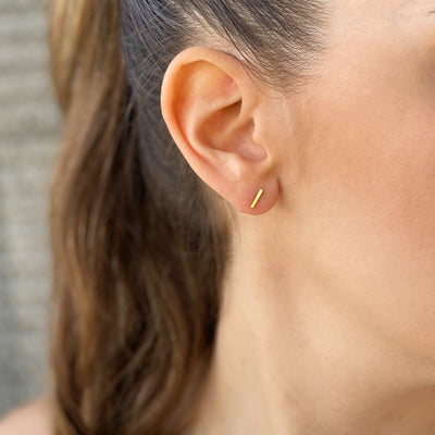 עגילים קטנים בצורת פס דק בגוון זהב מבריק על אוזן של דוגמנית